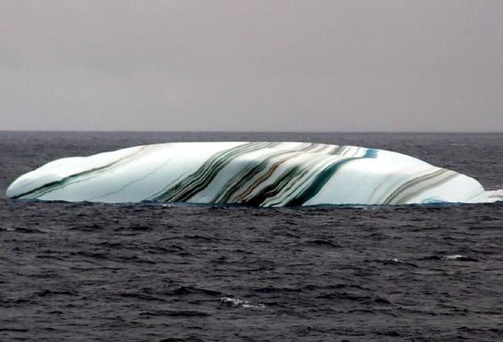 Some of the stripes formed when layers of the iceberg melted and refroze.  Others were created from the dust and soil picked up when the ice sheet that gave birth to the iceberg was sliding down an Antarctic hillside.