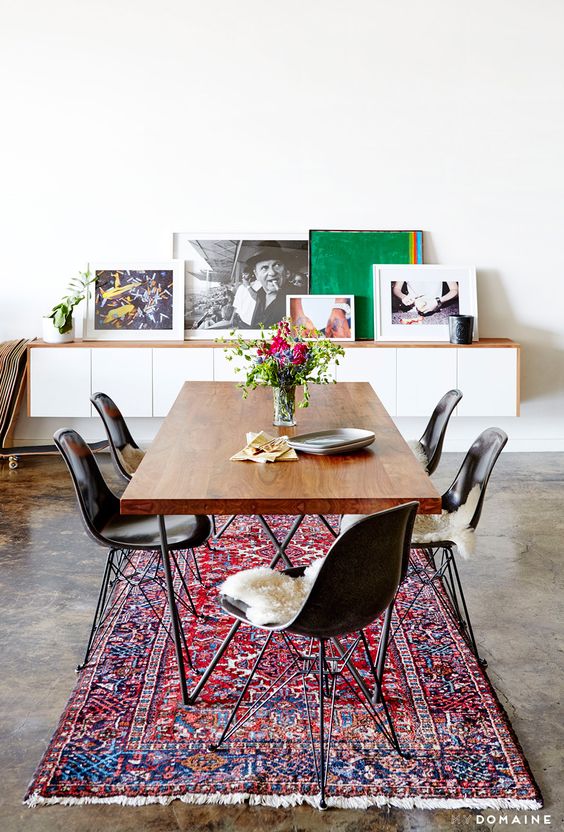 An industrial and modern dining space with leaning artwork, Persian rug, and wood dining table
