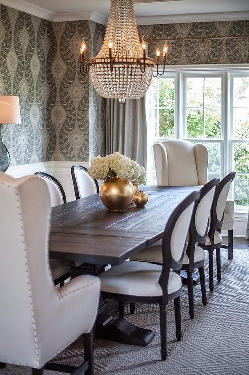 Black salvaged wood dining table, Restoration Hardware Salvaged Wood Trestle Rectangular Extension Dining Table, lined with black and white French round back dining chairs and wingback captain chairs placed at each end of the table atop a diamond print rug.