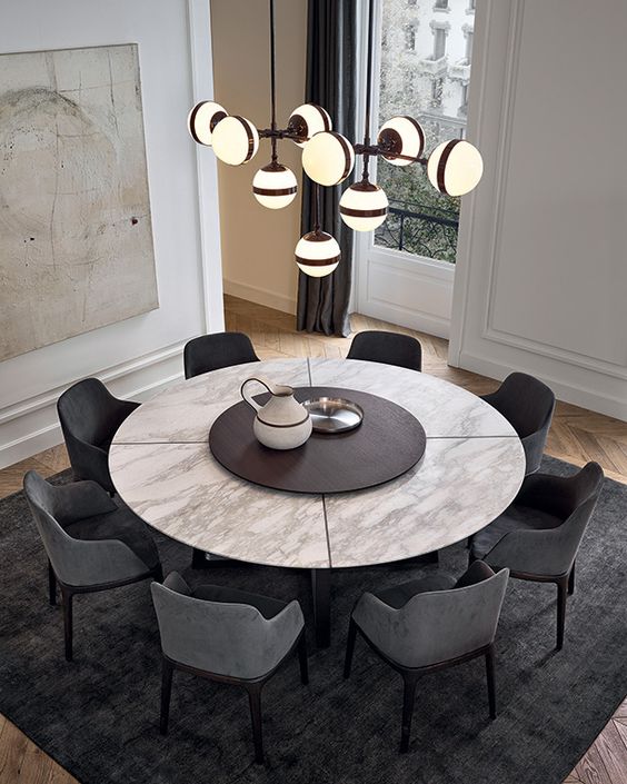 Concorde table in spessart oak, top in mat calacatta oro marble with central spinning tray in spessart oak. Grace armchairs in spessart oak and 5 grafite Nabuk leather. Onda pouf in 1401 oliva Persia removable velvet.