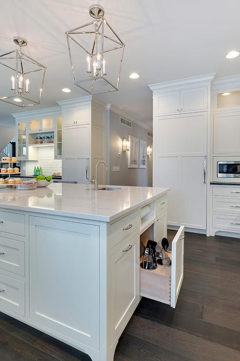 Gorgeous kitchen island sat upon stained oak hardwood floors features white shaker cabinets topped with a white marble countertop fitted with a curved prep sink and polished nickel faucet illuminated by two 4 light Darlana lanterns and recessed lighting.