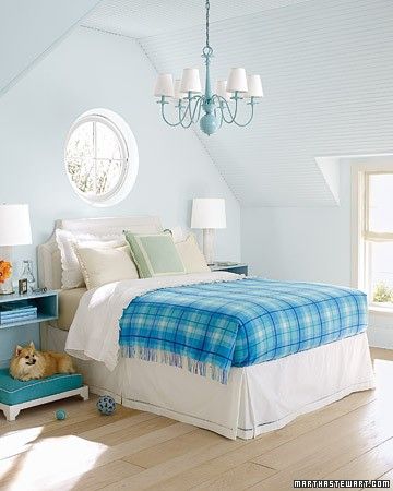 The key to enlivening a neutral room is to brighten it with several shades of the same color. In a mostly pale room, a plaid blanket makes a strong statement. The chandelier, the wall-mounted bedside tables, and the cushion on the dog bed reiterate the blanket's several shades of blue.