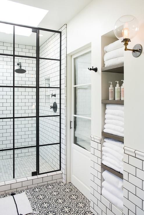 White and black bathroom boasts an alcove filled with shelves holding towels alongside a white and black floor in Cement Tile Shop Bordeaux Tiles.