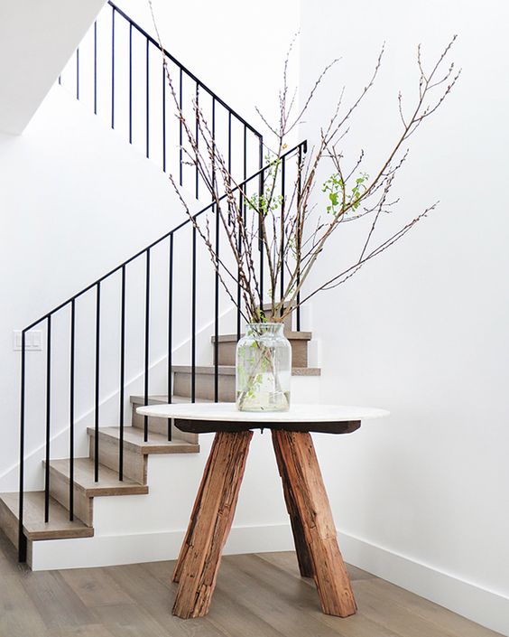 Entryway: decorative branches in glass vase on white marble-top table with wooden legs; solid timber floorboards and staircase; black metal balustrade