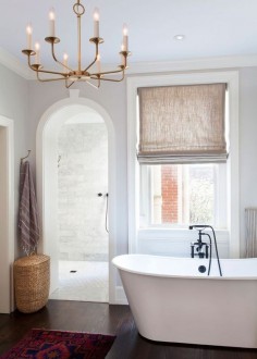 A gold light fixture and a linen Roman shade hang above a white soaking tub.