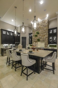 A large center island provides the perfect spot to eat in this gourmet kitchen. The stacked stone range hood brings a rustic quality to the space, while sleek black cabinets paired with neutral countertops create a warm, contemporary style.