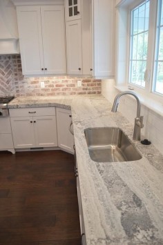 Amazing kitchen features a white shaker cabinets paired with gray quartzite countertops fitted with a curved stainless steel sink and a white subway tiled backsplash.