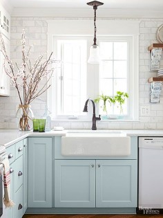 An enlarged window above the sink allows plenty of sunlight to stream into the cottage kitchen. An apron-front sink and oil-rubbed bronze faucet contribute vintage appeal. A marble-tile backsplash, installed by the homeowner, shimmers against pale blue base 