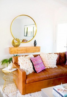 Bright boho living space with a leather sofa, a large rug, and a gold round mirror