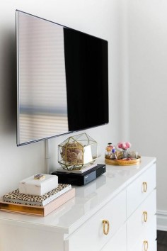 Chic bedroom features a flatscreen TV atop a white Ikea Malm Dresser adorned with gold ring hardware.