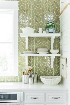 Coastal Living Showhouse - White and green kitchen features white cabinets paired with white quartz countertops and a ceiling height green herringbone tiled backsplash lined with stacked white shelves with corbels.