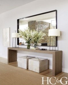 Contemporary neutral entry way design with oversized mirror and dual lamps and ottomans
