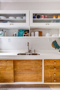 Cozinha branca com azulejos que imitam tijolinho branco, armários com vidro e madeira de demolição.