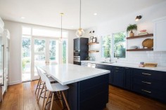Fabulous kitchen features navy blue shaker cabinets adorned with aged brass pulls paired with white quartz countertops that resemble marble and a white stacked tile backsplash.