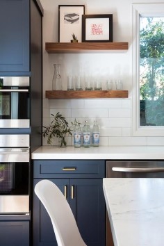 Fantastic kitchen features navy blue shaker cabinets adorned aged brass pulls paired with white quartz countertops that resemble marble and a white stacked tile backsplash.