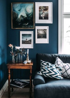 Living room with dark blue marine walls, layered art, and a vintage table