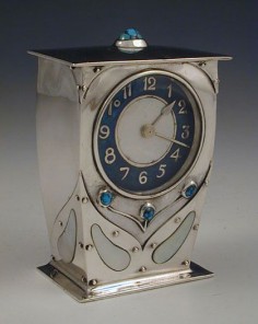 Manufacturer	Liberty & Co.  Designer	Archibald Knox  Description	Silver Arts & Crafts clock. Enamel on silver dial, with mother of pearl centre. Faux rivet decoration and mother of pearl inlay to front and sides Set with turquoise stones to top and front.  Country of Manufacture	England  Date	1911
