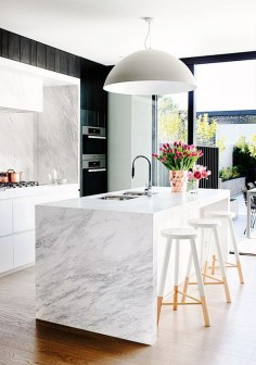 Marble kitchen with modern light fixture, beautiful flowers, and wood bar stools