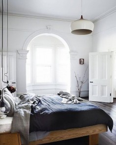 Minimalist bedroom with high ceilings, gray bedding, and a pendant light