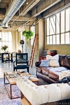 Open floor plan loft apartment with leather couch, ladder, wooden coffee table.