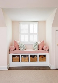 Pink girl's room features a nook filled with a built-in window seat fitted with open cubbies filled with woven baskets topped with a dusty pink linen cushion with white piping as well as matching bolster pillows, pink zigzag pillows in Quadrille Fabrics Petite Zig Zag and dalmatian print pillows in Thibaut Tanzania Fabric.