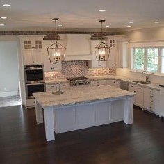 Red Brick Herringbone Cooktop Backsplash with oversized lantern pendants and white cabinets with hood in kitchen