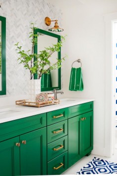 This gorgeous green-and-white bathroom is a preppy dream! Two mirrors and a double vanity make it easy for a pair of people to prepare for their day. Farmhouse-style fixtures light up the space, while a blue-and-white throw rug provides a bright contrast to the kelly green cabinets and accents.