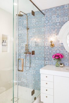 White and blue bathroom features a wall clad in blue Moroccan tiles, Fez Blue Vintage Moroccan Victorian Encaustic Effect Pattern Wall & Floor Tiles, lined with a white lacquered washstand adorned with aged brass knobs topped with thick white quartz and paired with an aged brass faucet placed under a white Mansard mirror.