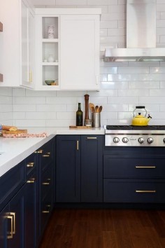 White and blue kitchen features white upper cabinets and navy blue lower cabinets adorned with aged brass pulls paired with white quartz countertops that resemble marble and a white stacked tile backsplash.