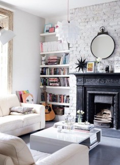 A bright white living room with modern furniture, a white painted brick wall and a black ornate architectural fireplace.