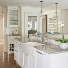 Beautiful kitchen features a white kitchen island topped with gray quartz fitted with a farmhouse sink and a vintage style faucet illuminated by Arteriors Caviar Pendants.