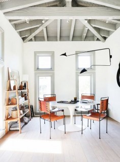 Minimalist dining space with gray accent paint features, leather stools, and a black sconce