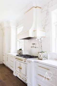 White and gold kitchen features white cabinets adorned with long gold pulls paired with Silestone countertops and backsplash that resemble white marble.
